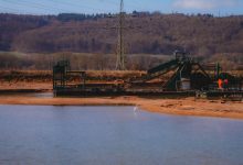 Operação de mineração a céu aberto próxima a um corpo d’água durante o dia