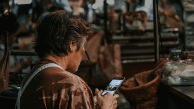 Mulher consulta o celular em meio ao movimento de um mercado.