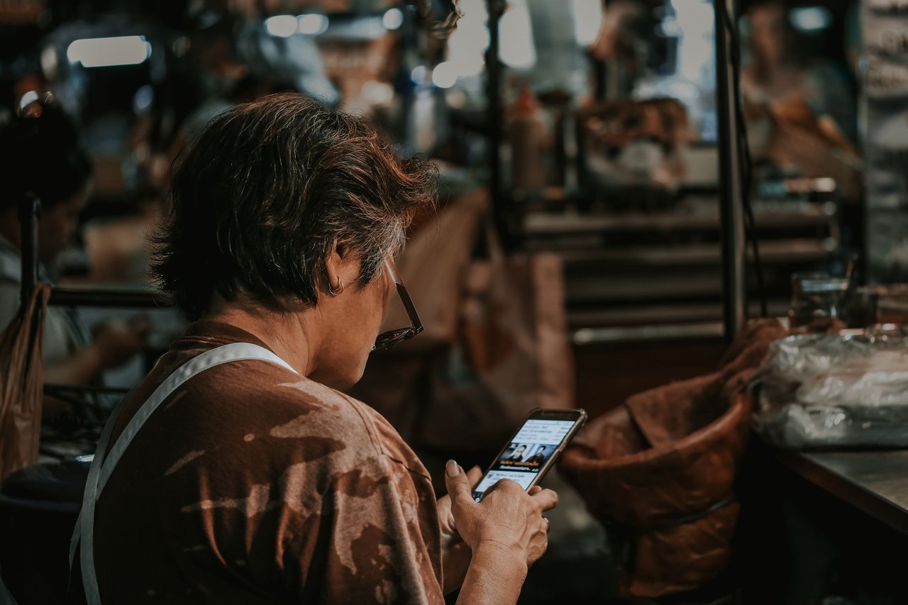 Mulher consulta o celular em meio ao movimento de um mercado.