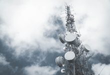 Torre metálica de telecomunicações com antenas e pratos de transmissão diante de um céu nublado.