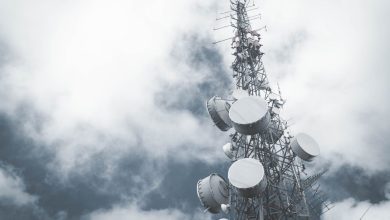 Torre metálica de telecomunicações com antenas e pratos de transmissão diante de um céu nublado.
