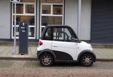 Carro elétrico branco e preto conectado a uma estação pública de recarga.