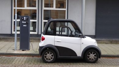 Carro elétrico branco e preto conectado a uma estação pública de recarga.