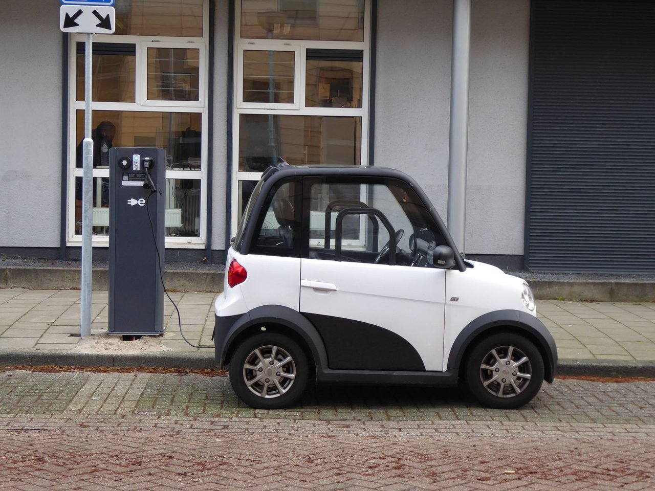 Carro elétrico branco e preto conectado a uma estação pública de recarga.