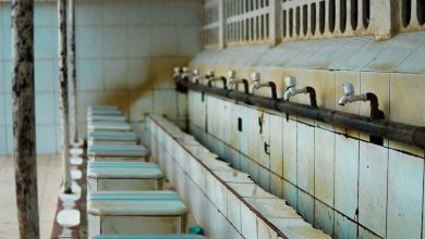 Área de lavagem revestida com azulejos e torneiras, sem pessoas.