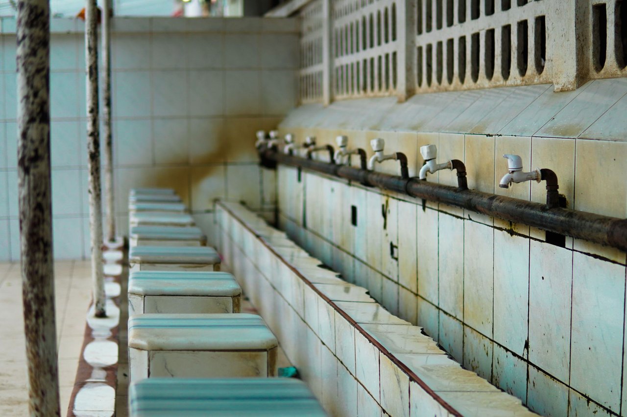 Área de lavagem revestida com azulejos e torneiras, sem pessoas.