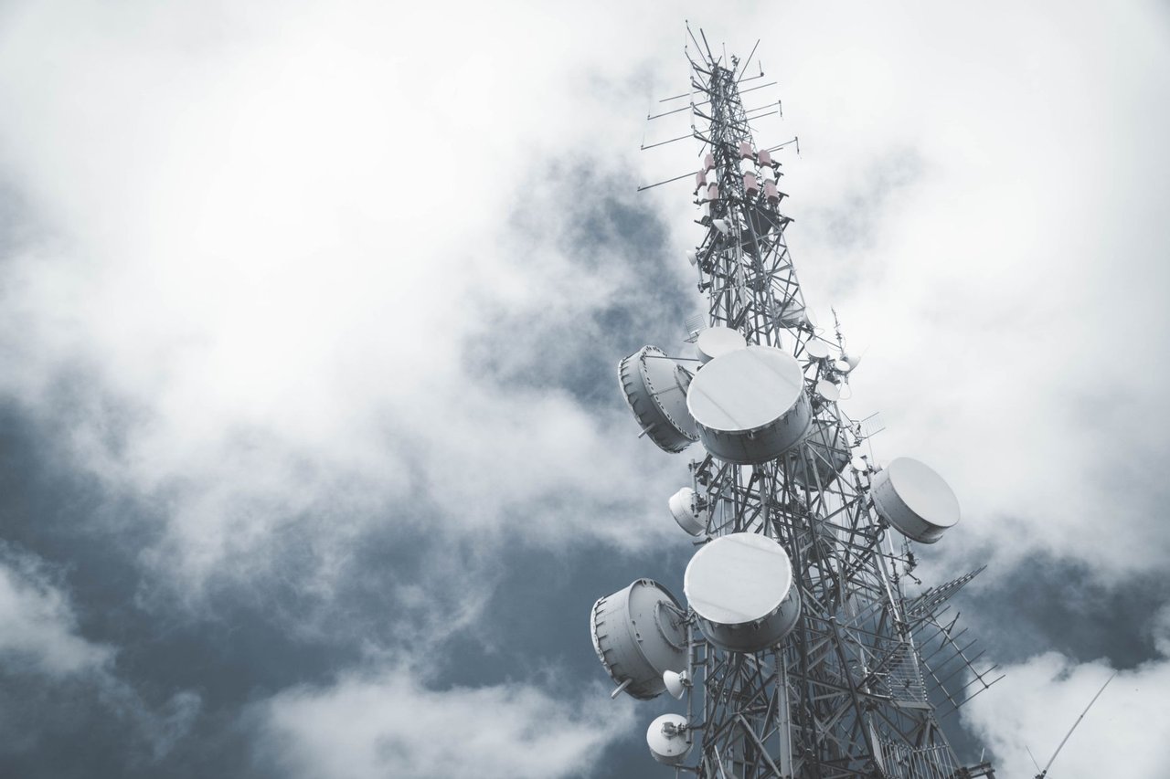 Torre metálica de telecomunicações com antenas e pratos de transmissão diante de um céu nublado.